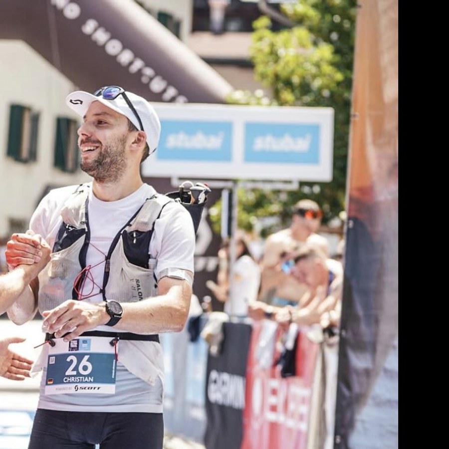 Christian smiling at the finish line of a trail running race, wearing race bib number 26